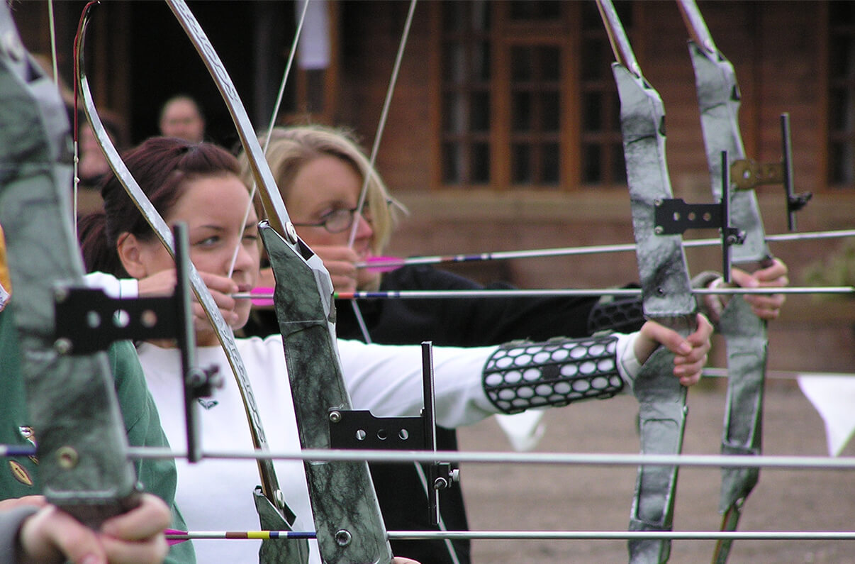 A group of women in a line, pulling back on a bow and arrow