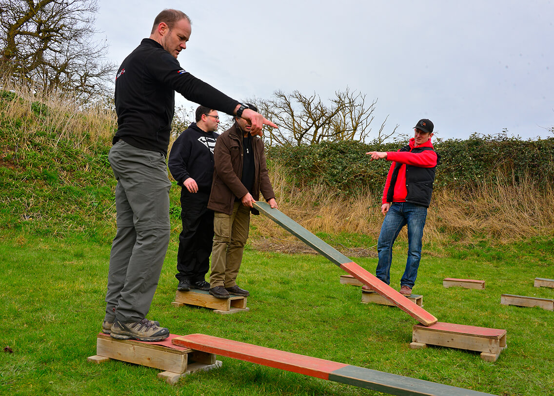 A group trying to cross platforms together using planks of wood